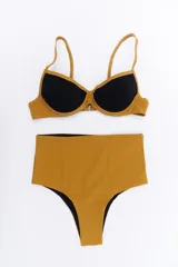 Bikini de dos piezas en combinación de colores negro y mostaza. El corpiño es de estilo triangular con base y breteles finos, mientras que la bombacha es de corte clásico con cintura alta en color negro.