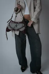 Bolso bandolera de cuero color borravino y tela a cuadros príncipe de Gales. Tiene correa ajustable, cierre metálico plateado y herrajes plateados.