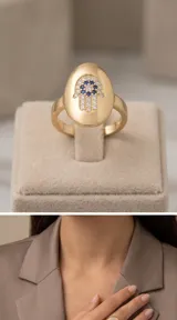 Anillo de plata 925 con baño de oro, de diseño ancho y ovalado en la parte superior, decorado con una mano de Fátima (Hamsa) engastada con circonias blancas y zirconias azules en el centro.