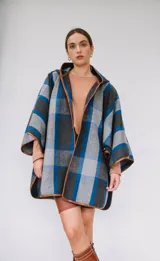 Ruana confeccionada en paño italiano con diseño a cuadros en tonos gris, azul y negro, con terminaciones ribeteadas en cuerina color camel y botón en las mangas.