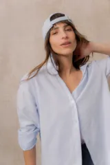 Camisa de calce amplio color celeste con delicadas rayas verticales, cuello camisero, mangas largas y abotonadura frontal.
