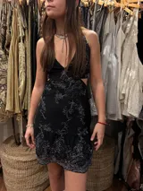 Vestido corto negro con estampado de plumas doradas, escote en V, breteles finos cruzados en la espalda, cut-outs laterales y volado en el ruedo.