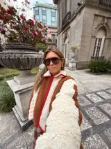 Campera de corderito con diseño de rayas verticales en colores marrón y crema, con cierre frontal y detalles de ribete en color rojo.
