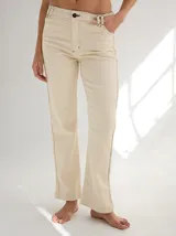 Pantalón de gabardina color beige, de corte recto, con bolsillos laterales y traseros. Se ajusta a la cintura con cinturón de cuero marrón.