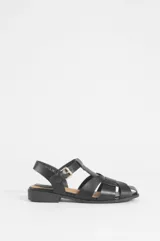 Sandalias planas negras estilo romano de cuero vegano, con diseño de tiras cruzadas, talón cerrado y hebilla metálica dorada ajustable en el tobillo.
