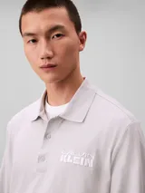 Chomba de manga larga Calvin Klein color gris, confeccionada en tejido jersey grueso aterciopelado de algodón. Cuenta con cuello clásico, cierre frontal con tres botones y logo de la marca bordado en relieve en el pecho.