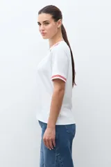 Remera blanca de algodón con cuello redondo y mangas cortas. Presenta bordados florales rojos en los hombros y en los bordes de las mangas.