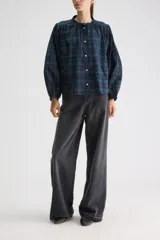 Blusa de calce relajado y silueta amplia, confeccionada en algodón liviano con estampado a cuadros en tonos azul marino y verde. Presenta cuello mao, cierre frontal con botones, hombros fruncidos y mangas largas con volumen que finalizan en puños elastizados.