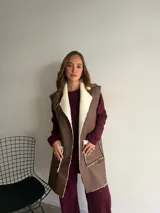 Chaleco largo de eco cuero color marrón con interior y detalles de corderito en solapas y bolsillos frontales.