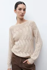 Sweater de punto color beige claro, con escote bote y tejido calado con diseño ondulado. Es de manga larga y corte recto.