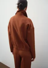Chaqueta color marrón terracota de cuello camisero, manga larga, bolsillos laterales y cierre frontal con cremallera.