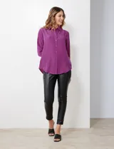 Camisa de satén color violeta, con cuello clásico, cierre frontal con botones, manga larga con puños anchos abotonados y bolsillo aplicado en el pecho.