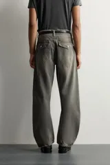 Jeans loose fit de hombre en denim de algodón color gris oscuro con efecto lavado. Presenta perneras con costuras giradas hacia los tobillos, tiro medio, cierre frontal con botones y bolsillos frontales con bolsillo cerillero.