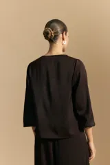 Blusa negra de satén con escote en V y detalle de volados frontales. Presenta mangas largas con puños abotonados y una silueta fluida.