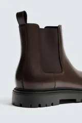 Bota tipo Chelsea de cuero color marrón oscuro, con paneles elásticos laterales, tirador trasero y suela track con volumen.