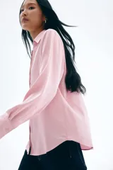 Blusa de manga larga color rosado pálido con acabado satinado. Presenta cuello clásico, escote en V con cierre de botones frontales y puños anchos.