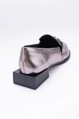 Mocasines de cuero en tono bronce metalizado, con detalle de aplique metálico dorado en el empeine y taco cuadrado bajo de madera.