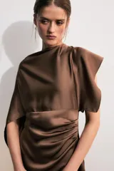 Vestido midi de satén color marrón, con cuello redondo, manga corta con capa fluida y cintura entallada con pliegues. Cuenta con falda recta con abertura en el bajo y cierre lateral con cremallera oculta.