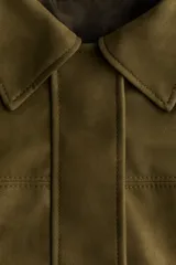 Campera bomber color verde militar de corte oversize, con cuello clásico, cierre frontal oculto bajo solapa y bolsillos laterales ribeteados.