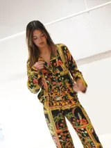 Conjunto de pijama de dos piezas con estampado floral y geométrico en tonos naranja, verde, amarillo y negro. Incluye camisa de manga larga con cuello y botones, y pantalón largo con cintura elástica.