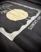 Hoodie oversize color negro con estampa en la espalda que presenta un diseño de palmeras y sol con la leyenda Sunset Life.