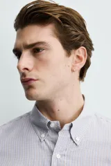 Camisa de corte regular fit confeccionada en tejido de algodón con estampado de microcuadros. Presenta cuello abotonado, manga larga con puños abotonados y cierre frontal de botones.