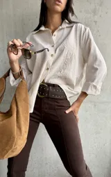Camisa clásica a rayas beige y blancas, con cuello camisero, botones frontales y bordado decorativo en el pecho.
