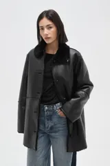 Tapado de eco-cuero negro con interior y cuello de piel sintética, cierre frontal con botones y diseño holgado.