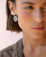 Aros tipo argolla de plata con dije circular de resina con diseño estampado de flores pequeñas en color bordó sobre fondo blanco.