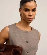 Chaleco regular color marrón claro con estampa de cuadros, confeccionado en punto roma, con cuello redondo, abotonado delantero con botones forrados y recorte en la bajo.