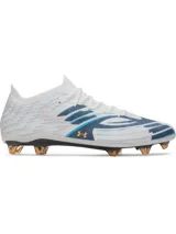 Championes de fútbol Under Armour Shadow Elite 4 Mach FG, color blanco con detalles en azul y naranja. Presentan una placa de fibra de carbono optimizada para mayor agilidad, microtextura háptica 3D en el empeine para un contacto óptimo con el balón y cuello elástico de punto para un ajuste ceñido.