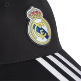 Gorra de béisbol Adidas del Real Madrid, color negro con visera curva y logo del club bordado en el frente. Presenta las tres líneas características de Adidas en blanco sobre la visera y cierre ajustable en la parte posterior.