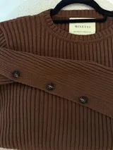 Sweater color camel de tejido de punto acanalado, con cuello redondo y botones decorativos en las mangas. Hecho en Uruguay.