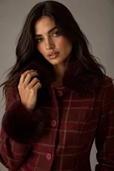 Chaqueta entallada de diseño clásico con estampado de cuadros escoceses en tonos bordó. Presenta cuello y puños con detalle de pelo sintético al tono, cierre frontal con botones y corte ajustado.