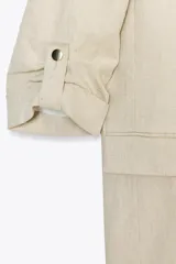 Blazer color beige confeccionada en lino, de corte recto, con cuello solapa, hombreras y mangas 3/4 con trabilla y botón dorado.