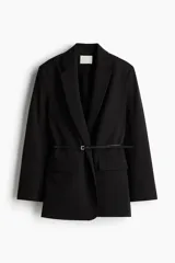 Blazer de sarga color negro con solapas de muesca, frente cruzado y cinturón fino ajustable con hebilla metálica. Presenta bolsillos delanteros ribeteados con solapa y diseño forrado.