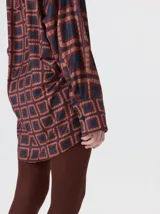 Camisa de seda con cuello camisero, manga larga y bolsillo frontal. Presenta un diseño estampado geométrico de cuadrados en tonos marrones y azul oscuro.
