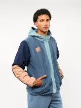 Campera de polar con capucha, cierre frontal completo y diseño en bloques de color azul y azul marino. Presenta detalles en nylon en la zona del cierre y la capucha, con logo de la marca aplicado en el pecho.