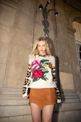Sweater artesanal tejido de lana color crudo, con diseño de rosas bordadas en el frente y mangas con patrón a cuadros de crochet en tonos tierra. Cuenta con cuello redondo y calce holgado.