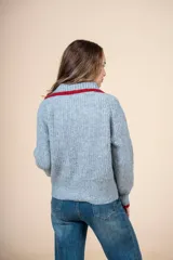 Cárdigan de punto gris con cuello camisero y detalles en rojo en cuello y puños. Cierre frontal con botones.