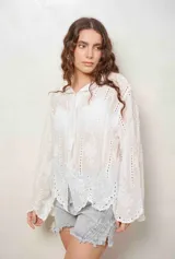 Camisa blanca de manga larga con bordados florales y detalles de ojales, cuello camisero y cierre frontal con botones ocultos.