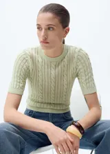 Jersey de punto color verde menta, con diseño de trenzas y detalles calados. Presenta cuello redondo, manga corta y terminaciones elásticas acanaladas.
