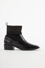 Bota de caña media combinada, con puntera y talón en cuero negro y caña de tejido de punto acanalado elástico. Cuenta con taco cuadrado bajo y tirador trasero.