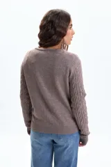 Saco de punto color tostado, con diseño de trenzas verticales en todo el cuerpo y mangas. Tiene cuello redondo y cierre frontal con botones pequeños.