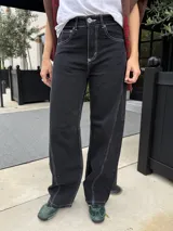 Pantalón de jean de corte recto y tiro medio, con un acabado de teñido ácido en tonos oscuros. Presenta bolsillos traseros con bordados decorativos en color negro y una etiqueta de cuero en la cintura.