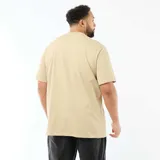 Remera de algodón color beige con cuello en V y manga corta. Presenta un corte holgado y una etiqueta decorativa pequeña en el borde inferior.