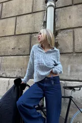 Polo de punto celeste con patrón trenzado, cuello tipo polo abierto y mangas largas. Presenta logos estampados en el pecho y diseño de estilo deportivo retro.