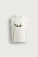 Camiseta tank blanca de corte relajado, con textura en relieve, cuello redondo y sisas amplias. Cuenta con un diseño bordado y estampado en el centro del pecho con las inscripciones "Slow Vibes" y "After Hours" en tonos verde y negro.