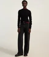 Blusa de punto acanalado en color beige, con cuello alto y mangas largas. Presenta un diseño ajustado al cuerpo con un detalle de borde en color marrón en el cuello y en el ruedo.