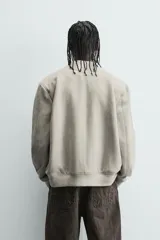 Cazadora bomber negra de corte regular fit, confeccionada en tejido efecto ante. Cuenta con cuello, puños y bajo en rib elástico, manga larga, bolsillos de vivo en la cadera y un bolsillo interior. Cierre frontal con cremallera.